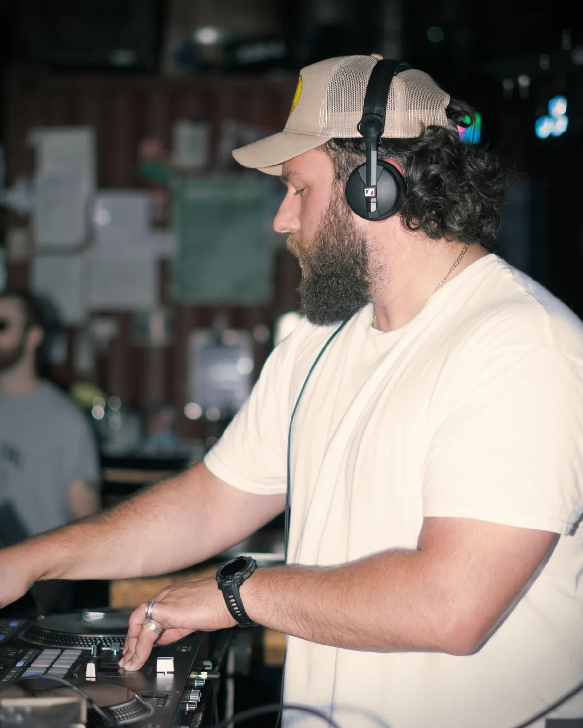 Kris Falco mixing on CDJs at a Kelowna bar, trucker cap and headphones on